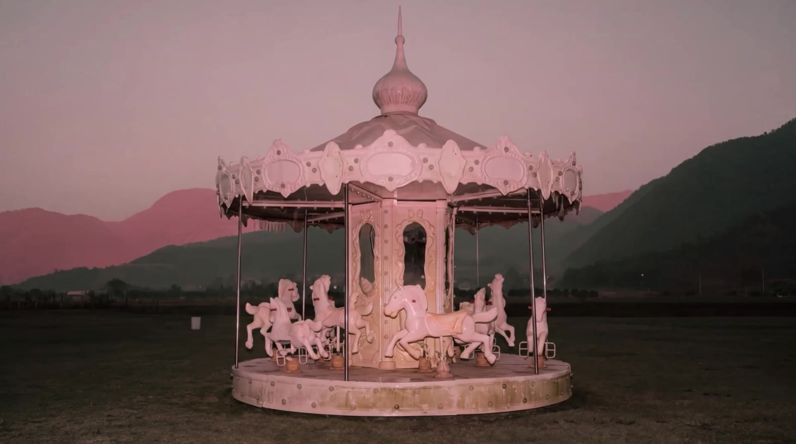 Weite Einstellung eines blassen Vintage-Karussells vor Bergen in der Dämmerung.